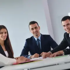 Grupa ludzi w garniturach siedzi przy stole, dyskutując nad dokumentami.