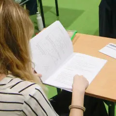 Dziewczyna z blond włosami czyta arkusz z zadaniami matematycznymi.