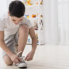 Chłopiec klęczy i zapina rzepy w białych butach sportowych.
