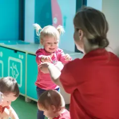 Nauczycielka w czerwonej koszulce bawi się z dziećmi w sali przedszkolnej.