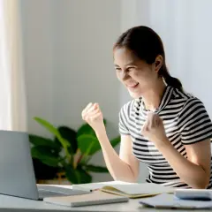 Uśmiechnięta młoda kobieta cieszy się z sukcesu przy laptopie.