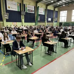 Uczniowie siedzą przy ławkach w sali gimnastycznej podczas egzaminu.