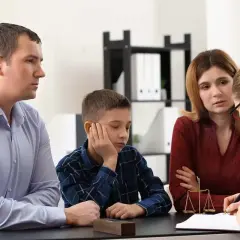 Rodzina z dzieckiem rozmawia z prawniczką przy biurku, na którym stoi waga sprawiedliwości.