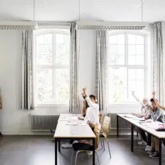 Nauczyciel stoi przed klasą, w której uczniowie podnoszą ręce.