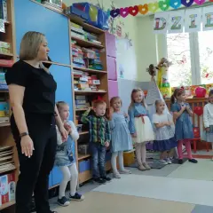 Nauczycielka i dzieci w przedszkolu, na półkach gry i zabawki.