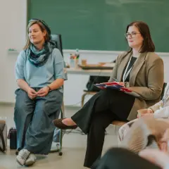 Grupa osób siedzi w kręgu, słuchając prelegenta.