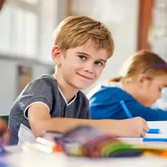 Uśmiechnięty chłopiec w klasie, gdzie dzieci z różnymi specjalne potrzeby edukacyjne uczą się razem.