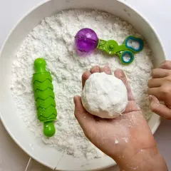 Dziecko tworzy kulkę z białej masy sensorycznej, obok wałek i nożyczki do zabawy.