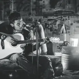 Młody muzyk gra na gitarze akustycznej, tworząc różne rodzaje muzyki w surowym, industrialnym otoczeniu.