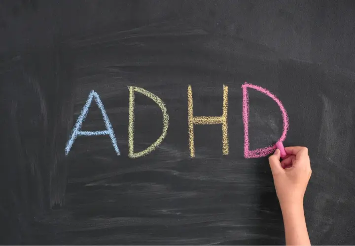Napis "ADHD" kredą na tablicy, pisany przez rękę.