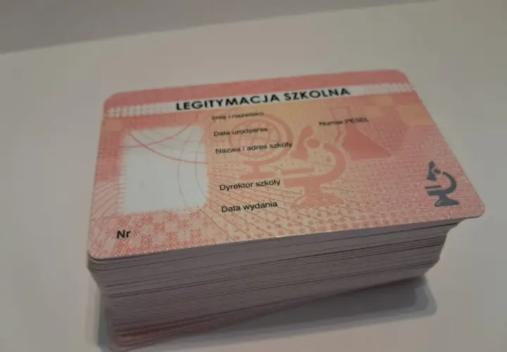Stos nowych legitymacji szkolnych z widocznym napisem "LEGITYMACJA SZKOLNA" i mikroskopem.