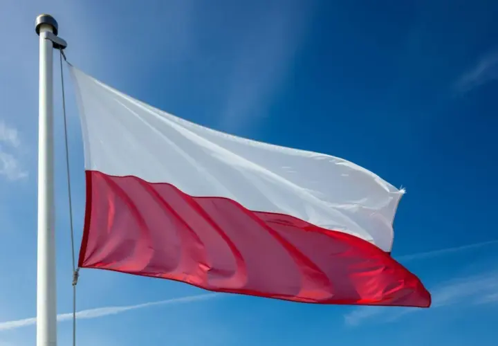 Polska flaga powiewa na maszcie na tle błękitnego nieba.
