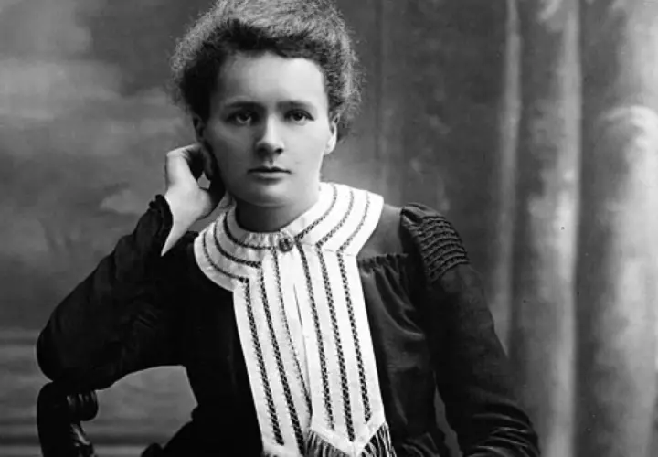Czarno-białe zdjęcie Marii Skłodowskiej-Curie w eleganckiej sukni z ozdobnym kołnierzem.