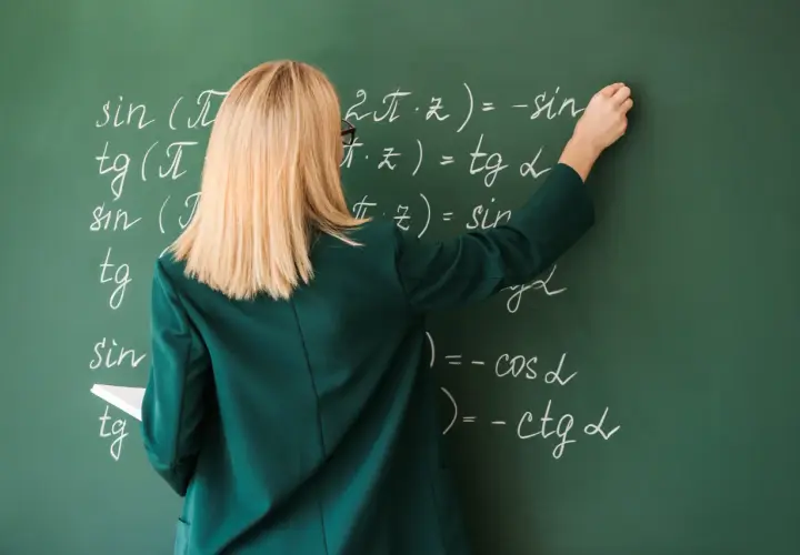 Nauczycielka pisze kredą wzory matematyczne na zielonej tablicy.