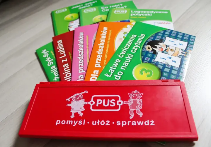 Czerwone pudełko z zabawkami edukacyjnymi PUS i kolorowe książeczki.