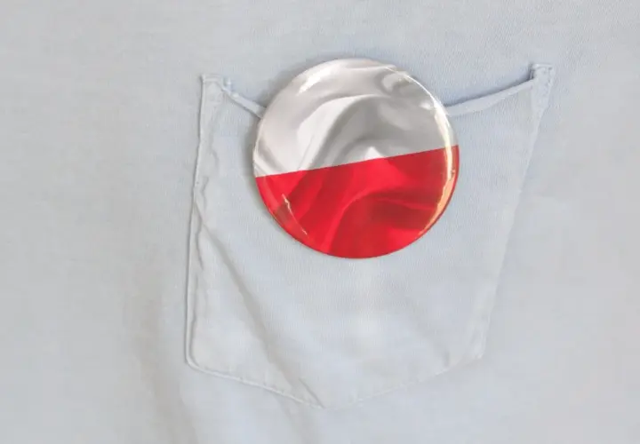 Okrągła przypinka z polską flagą wpięta w kieszeń jasnoniebieskiej koszuli.
