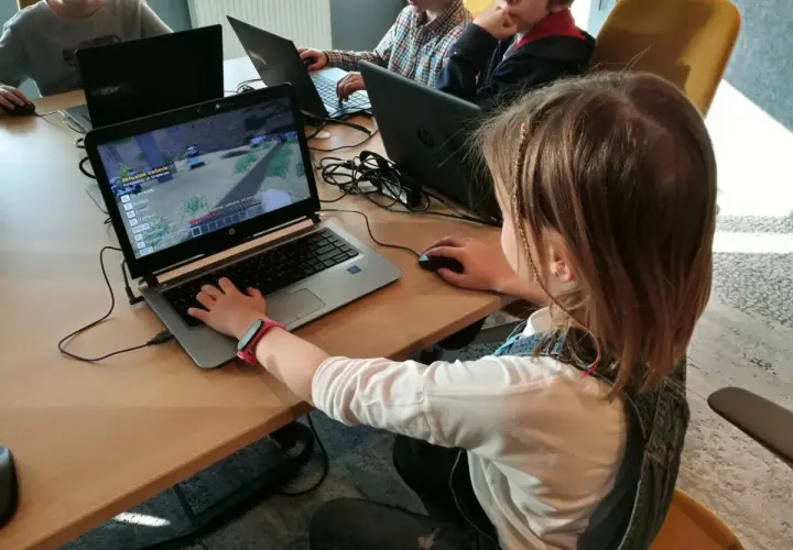 Dzieci grają w grę komputerową na laptopach podczas lekcji kodowania.