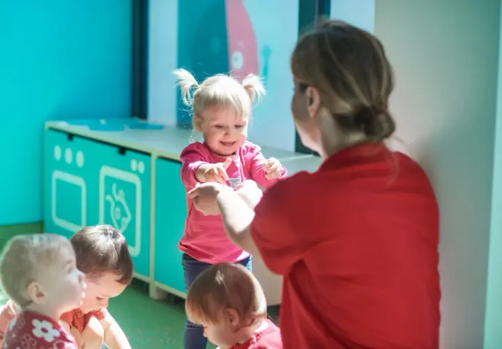 Nauczycielka w czerwonej koszulce bawi się z dziećmi w sali przedszkolnej.