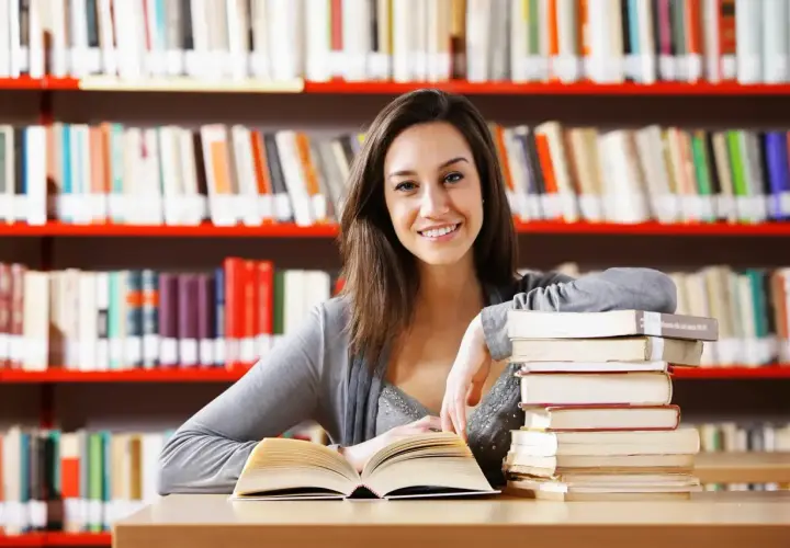 Uśmiechnięta studentka z książkami w bibliotece.