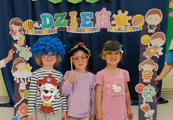 Dzieci w przedszkolu w strojach i z rekwizytami pozują do zdjęcia na tle dekoracji z napisem "Dzień Dziecka".