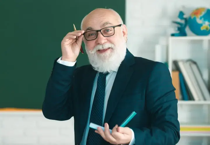 Uśmiechnięty starszy nauczyciel w okularach i garniturze trzyma długopis i marker.