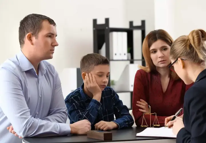 Rodzina z dzieckiem rozmawia z prawniczką przy biurku, na którym stoi waga sprawiedliwości.