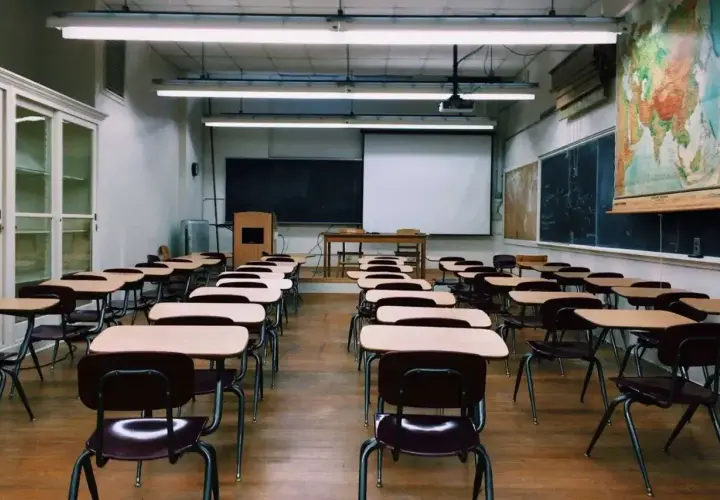 Pusta sala lekcyjna z rzędami ławek i krzeseł, tablicą i mapą świata.