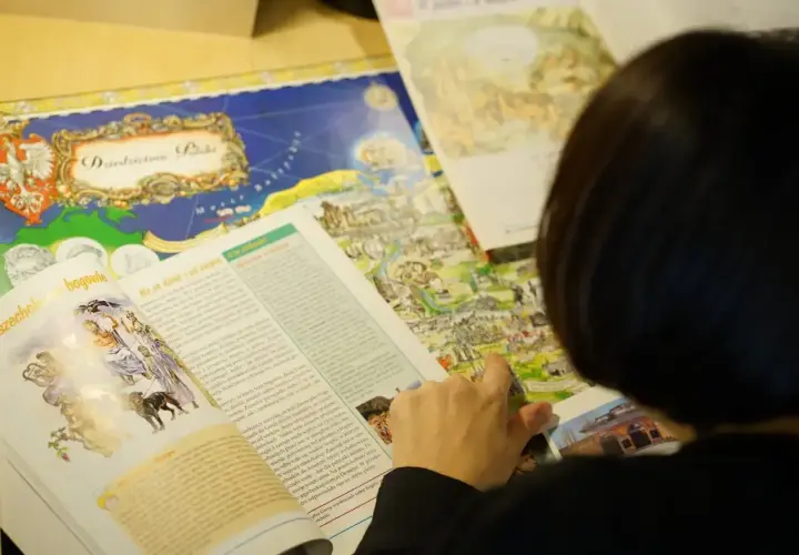 Osoba przegląda książkę z mapą Polski i ilustracjami mitologicznymi.