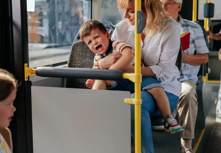 Płaczące dziecko na rękach matki w autobusie, obok siedzi starszy mężczyzna.
