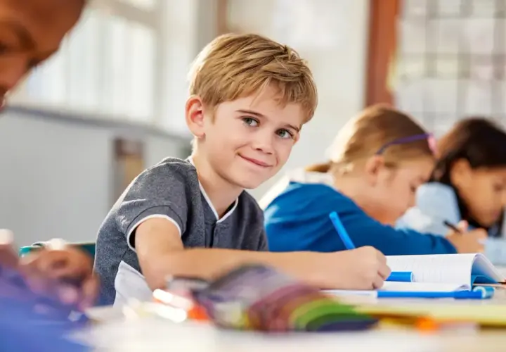 Uśmiechnięty chłopiec w klasie, gdzie dzieci z różnymi specjalne potrzeby edukacyjne uczą się razem.
