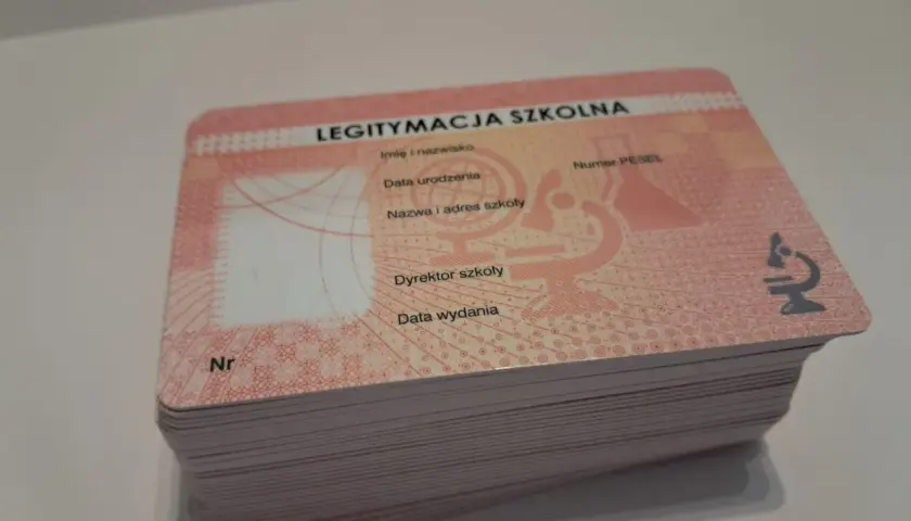 Stos nowych legitymacji szkolnych z widocznym napisem "LEGITYMACJA SZKOLNA" i mikroskopem.