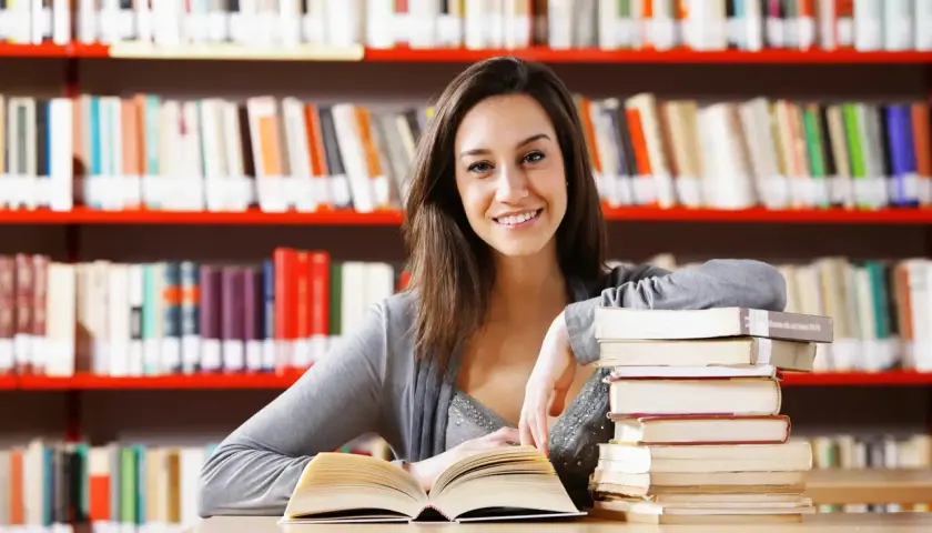 Uśmiechnięta studentka z książkami w bibliotece.