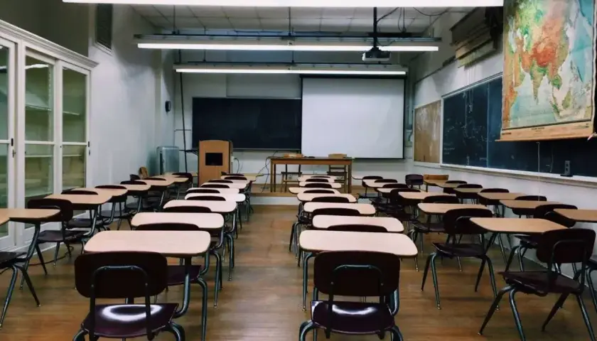 Pusta sala lekcyjna z rzędami ławek i krzeseł, tablicą i mapą świata.