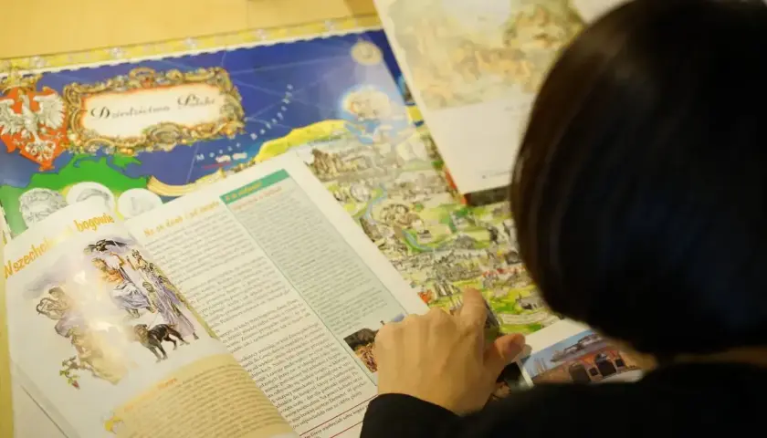 Osoba przegląda książkę z mapą Polski i ilustracjami mitologicznymi.