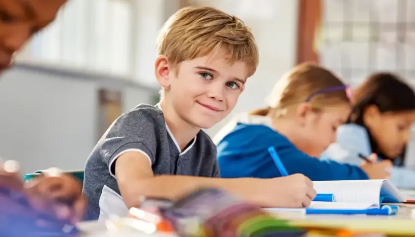 Uśmiechnięty chłopiec w klasie, gdzie dzieci z różnymi specjalne potrzeby edukacyjne uczą się razem.