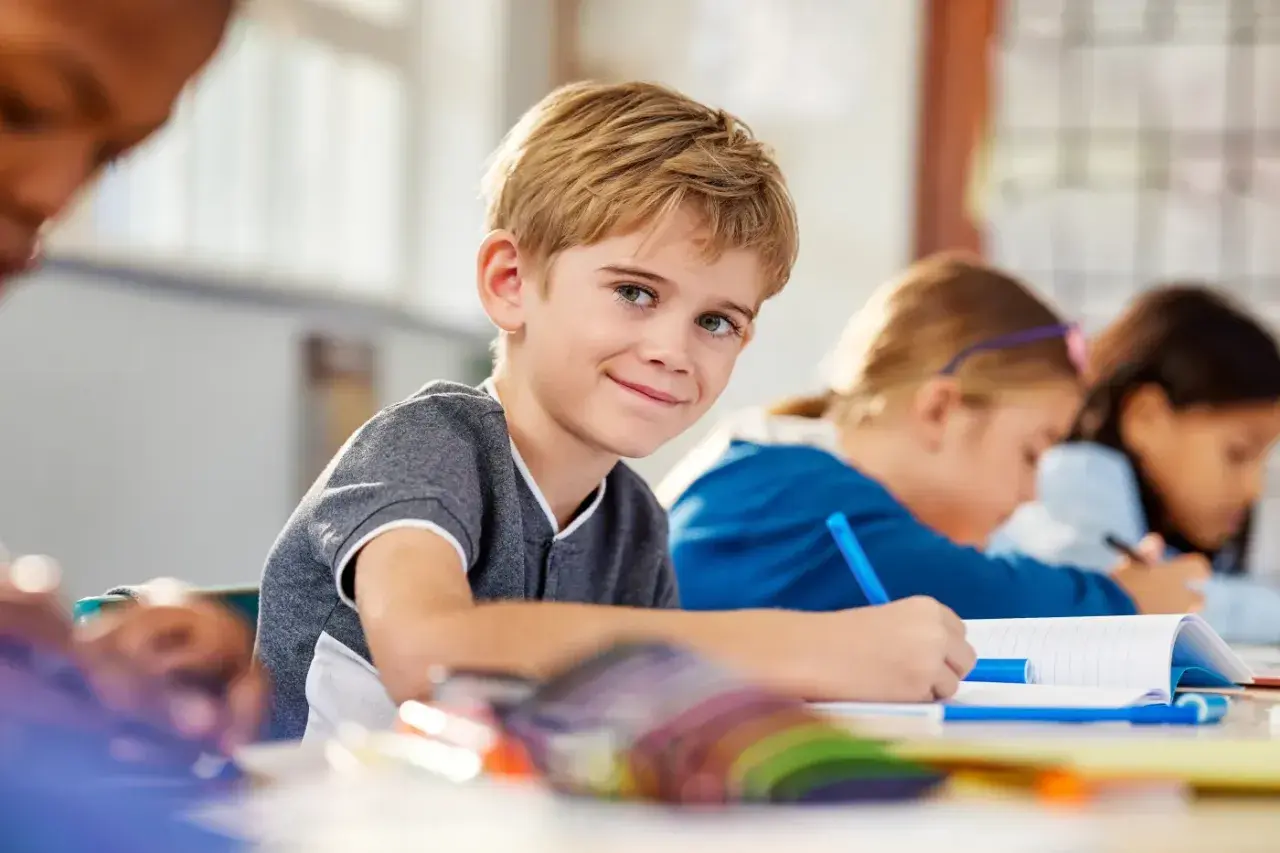 Uśmiechnięty chłopiec w klasie, gdzie dzieci z różnymi specjalne potrzeby edukacyjne uczą się razem.