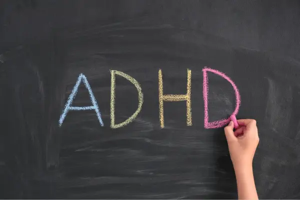 Napis "ADHD" kredą na tablicy, pisany przez rękę.