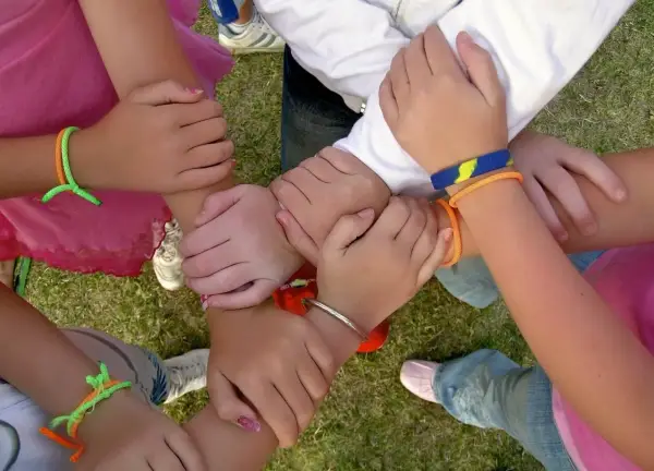 Dzieci trzymają się za ręce, tworząc okrąg. Mają na rękach kolorowe bransoletki.